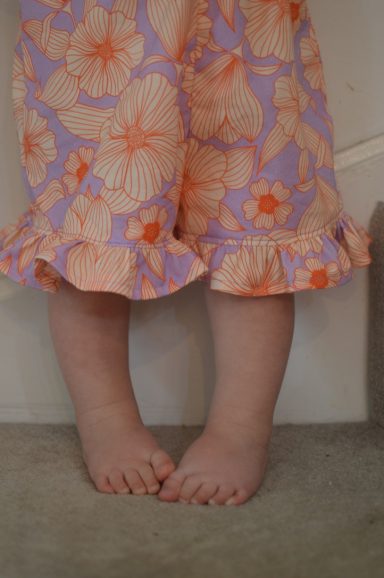 Tiny Folk Patterns The picture of a toddler's legs, wearing a homemade romper with frill around the shorts in a funky orange and purple pattern.